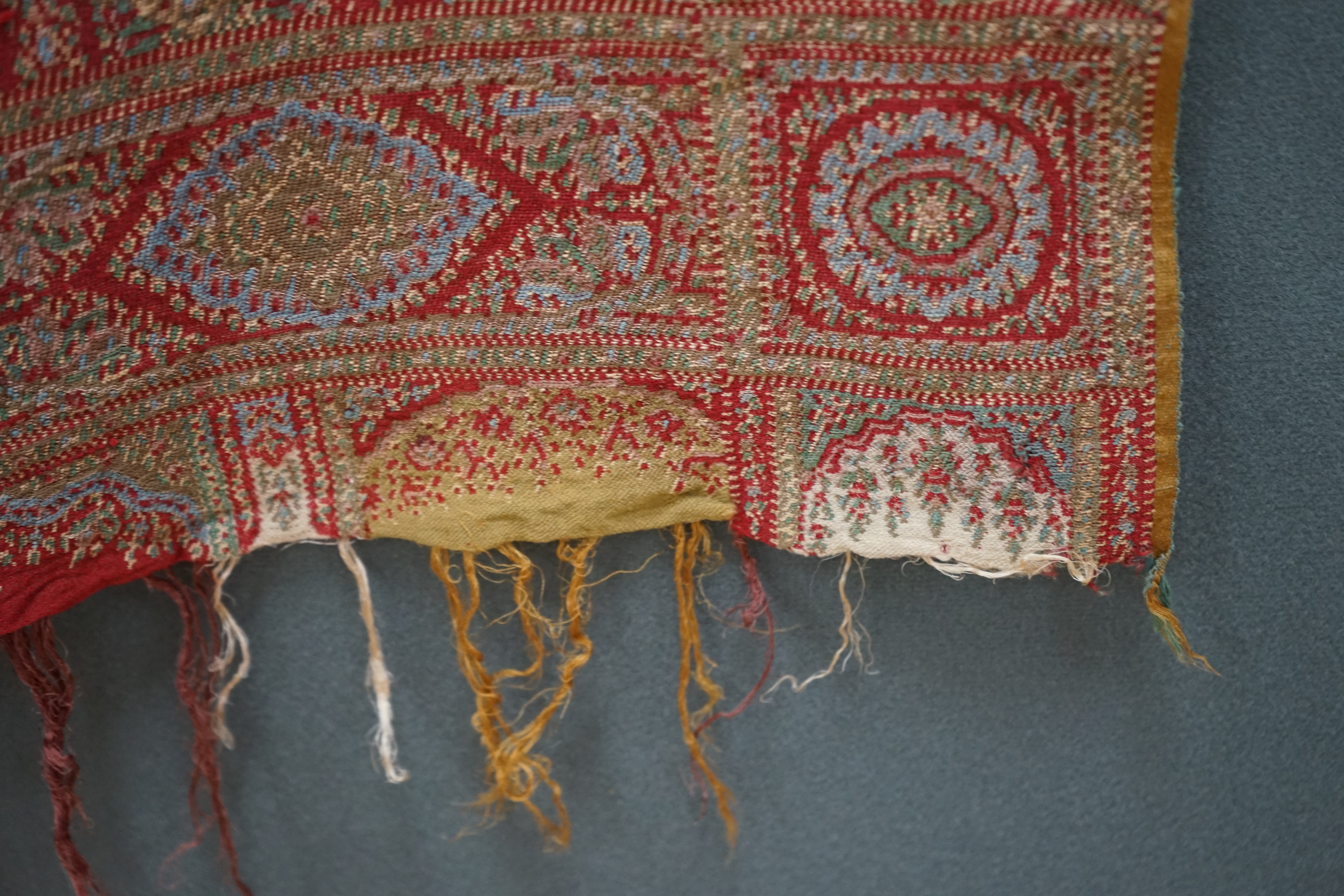 A 19th century wool and silk woven Paisley shawl, woven in a diagonal tear drop design, in reds, blues, greens, creams and ochres, with an all round woven border, tasselling both ends, 320cm long x 162cm wide. Condition